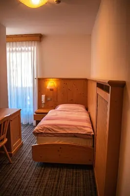 a bedroom with a bed and a desk and a window at Albergo Canazei in Canazei