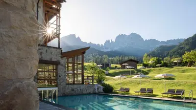 a resort with a pool and mountains in the background at Cyprianerhof Dolomit Resort in Tires