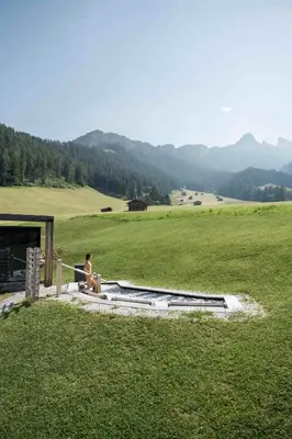 a person sitting on a ledge in a field at Cyprianerhof Dolomit Resort in Tires