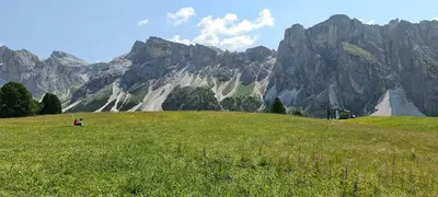 a person sitting on a grassy hill in front of a mountain at App. Lino nel cuore di Ortisei - casa dell'800 in Ortisei