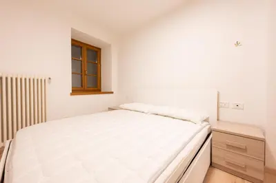 a white bedroom with a large bed and a window at Cesa Meida 2A in Pozza di Fassa