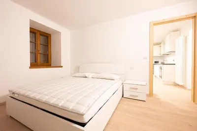a white bedroom with a bed and a kitchen at Cesa Meida 2B in Pozza di Fassa