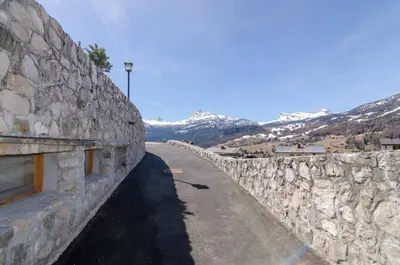 a stone wall next to a road with snowy mountains at Charming Studio in Chiave