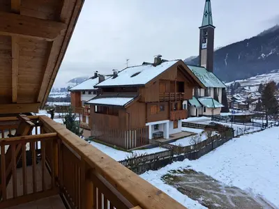 a wooden building with a clock tower in the snow at Villa San Carlo in Pozza di Fassa