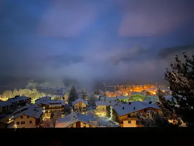 a town with snow covered roofs in a city at night at Encia's Home Dolomiti in Castello di Fiemme