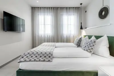 a white bedroom with a large bed and a flat screen tv at Villa Stubai Garden Suite in Merano