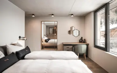 two beds in a bedroom with a desk and a mirror at Avita Loft by Avita suites to relax in Santa Cristina in Val Gardena