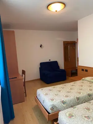 a bedroom with two beds and a blue chair at Garní Ladinia in Pescul