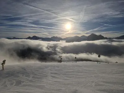 a person standing on a snow covered slope with the sun and clouds at M&M-Apartment in Brunico
