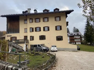 a large building with cars parked in front of it at Casa Da l Oio in Cortina dʼAmpezzo