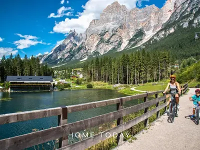 a woman and child riding bikes on a bridge near a lake at Hometoday - Appartamento nel cuore di San Vito di Cadore in San Vito di Cadore