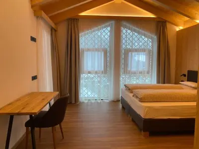 a bedroom with a bed and a table and windows at Les Ciases Chalets Dolomites in San Vigilio Di Marebbe