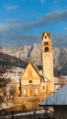 a church with a clock tower in front of mountains at Alessandro's Home in Carano