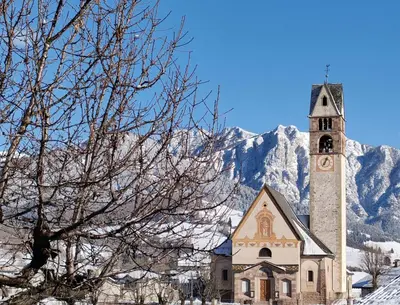 a church with a clock tower in front of a mountain at Alessandro's Home in Carano