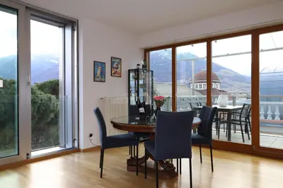 a dining room with a table and chairs and windows at Luxus Penthouse mit Terrasse, Garage, Fahrradraum und Infrarotsauna in Merano