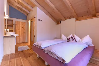 a bedroom with a bed with white sheets and a wooden ceiling at B&B Mas de Lagorae in Tesero