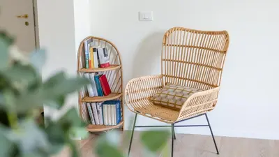a wicker chair and a book shelf with books at Italyescapes Emma 22 in Merano