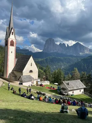 a group of people sitting in the grass in front of a church at Apartment Cesa Collina Superior in Ortisei