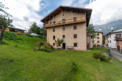 a building with a balcony on top of a green field at Appartamento Sant Antonio in Canale dʼAgordo