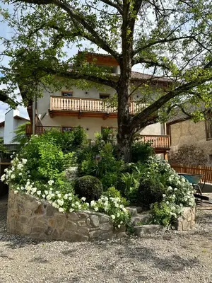 a tree in a garden with flowers in front of a house at Landhaus Breitenberg in Lana