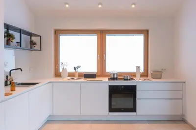a kitchen with white cabinets and two large windows at Ciasa Plandros Apartments in La Valle