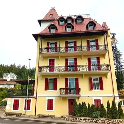 a yellow building with red windows and a balcony at Hotel Regina del Bosco in Ronzone