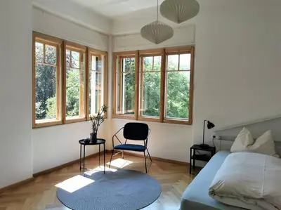 a bedroom with a bed and a chair and windows at Cityappartment Villa Landeck in Merano