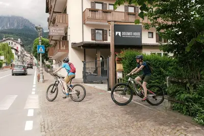 two people riding bikes down a street next to a building at Dolomitihouse NOGHERA in Fiera di Primiero