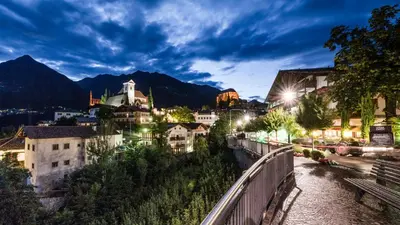 a city at night with mountains in the background at Natur Residence Kaiser Hans in Schenna