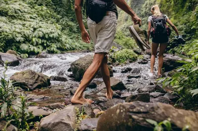 a man and woman walking across rocks in a stream at Garden Apartment Untermühle in Bressanone
