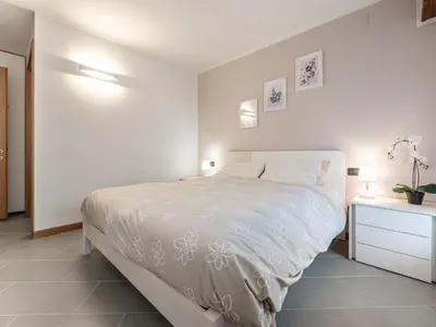 a white bedroom with a bed and a night stand at Apartment Condominio Giulia by Interhome in Alba di Canazei