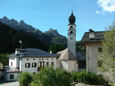 a building with a clock tower with mountains in the background at Da Carla Dolomiti Val di Zoldo in Val di Zoldo