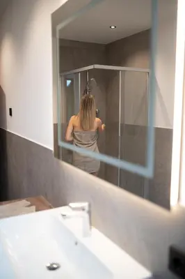 a woman is standing in a shower in a mirror at Alpenglow Apartments in Collalbo